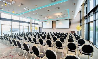 a conference room with rows of chairs arranged in a semicircle , and a projector screen mounted on the wall at Leonardo Offenbach Frankfurt