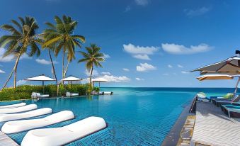 a large swimming pool with white lounge chairs and umbrellas in front of the ocean at Fushifaru Maldives