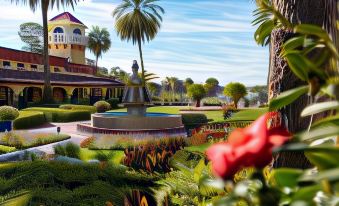a tropical garden with palm trees , flowers , and a fountain , set against a backdrop of buildings at Mission Inn Resort & Club