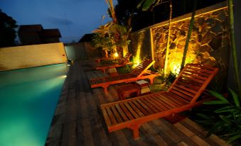 a wooden deck with several lounge chairs and a swimming pool , lit by lights at night at favehotel Rembang