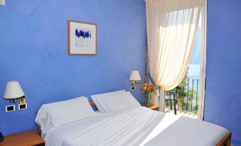 a bedroom with a blue wall , white bed linens , and a window looking out onto the ocean at Hotel Orso Bruno