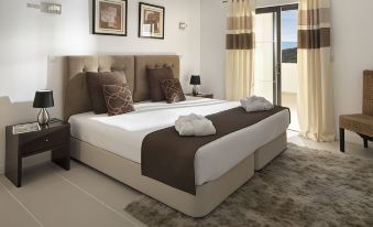 a large bed with a brown and white comforter is in a room with a window at Belmar Spa & Beach Resort