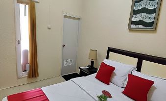 a clean and well - organized hotel room with a red bed , white sheets , and a lamp on the nightstand at Bakom Inn Syariah