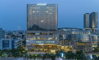 "a large building with a sign that says "" swissotel "" is surrounded by trees and other buildings" at Swissôtel Jakarta PIK Avenue