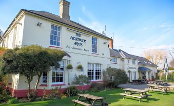 "a white building with a sign that says "" the mortimer arms "" has benches and tables outside" at The Mortimer Arms