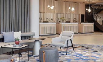 a modern hotel lobby with a check - in desk and a seating area with chairs and a table at Courtyard Basel