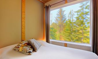 a bed with a white sheet and a pillow is next to a window overlooking trees at Woodland Cabins