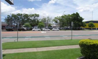 a street with cars parked on the side and a green grassy area in front at Raintree Motel