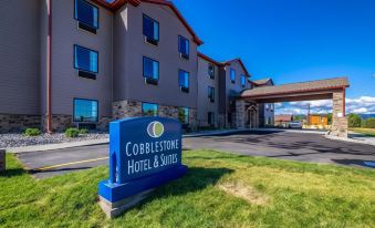 a large blue sign for the cobblestone hotel & suites is displayed in front of a gray building with the sign prominently displayed at Cobblestone Hotel & Suites - Victor