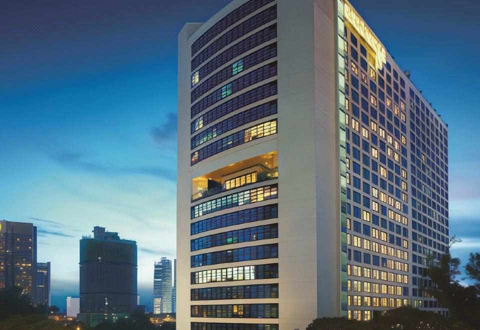 a tall , modern building with many windows is illuminated at night against the backdrop of a city skyline at Hotel Maya Kuala Lumpur City Centre