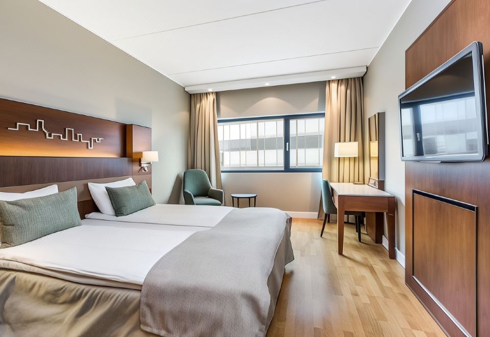 a modern hotel room with a large bed , wooden floors , and a desk area , as well as a window with curtains at Quality Hotel Fredrikstad