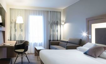 a modern hotel room with a white bed , couch , and dining table , all decorated in light colors at Novotel Château de Versailles