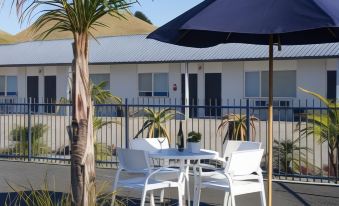 a patio area with a table , chairs , and an umbrella set up in front of a motel at Motel Oasis