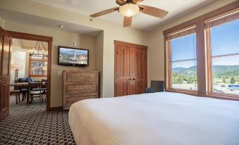 a large bed with a white comforter is in the center of a room with a television and dresser at The Village at Palisades Tahoe