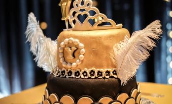 a black and gold birthday cake with a crown on top , surrounded by feathers and adorned with gold at Aston Imperial Bekasi Hotel & Conference Center