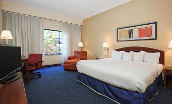 a large bed with white linens is in a room with blue carpeting and chairs at Courtyard Flint Grand Blanc