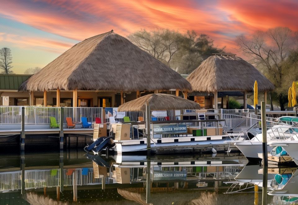 a row of boats docked next to a beach , with a thatched - roof building in the background at Ramada by Wyndham Sarasota Waterfront