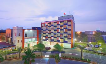 a modern , multi - colored building with a red flag on top is surrounded by palm trees and other buildings at Metland Hotel Bekasi