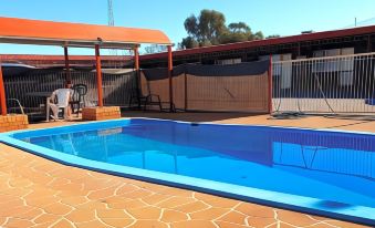 a blue swimming pool surrounded by a patio area , with a fence and chairs nearby at Ardeanal Motel