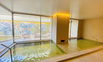 a modern indoor swimming pool with a view of an outdoor lounge area through large windows at Loisir Hotel Naha
