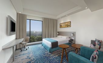 a modern hotel room with a large bed , blue and white striped rug , wooden nightstands , and a window offering a view of the city at Holiday Inn Express Kolkata Airport