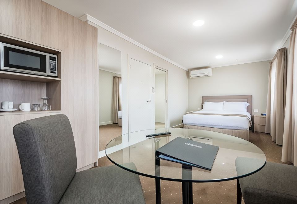 a modern hotel room with a glass coffee table , gray chairs , and a bed in the background at The Lighthouse Hotel