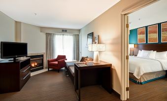 a cozy hotel room with a fireplace , red armchair , and a dining table with a laptop at Residence Inn Dayton Beavercreek