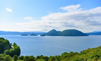 A large body of water is surrounded by trees and bushes, with mountains in the background at Hoshino Resorts KAI Poroto