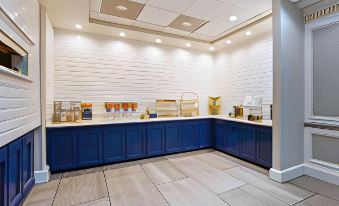 a well - lit room with white brick walls , blue cabinets , and a variety of food items on display at Luxor Inn & Suites, a Travelodge by Wyndham