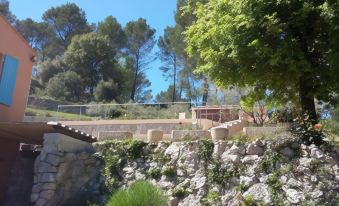 a stone wall with a dirt road leading to a building , surrounded by trees and bushes at La Roque