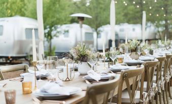 a long wooden table is set with white plates , wine glasses , and candles for an outdoor event at AutoCamp Yosemite