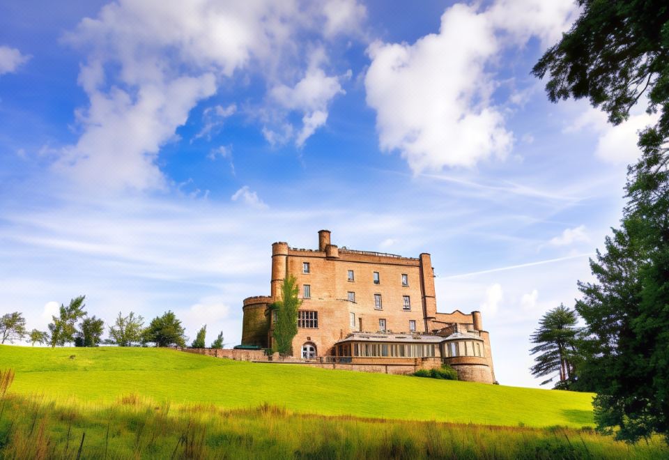 a large stone building , possibly a castle or a fortress , surrounded by lush green grass and trees at Dalhousie Castle Hotel