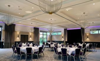 a large , well - lit conference room with multiple round tables and chairs set up for a meeting at Denham Grove