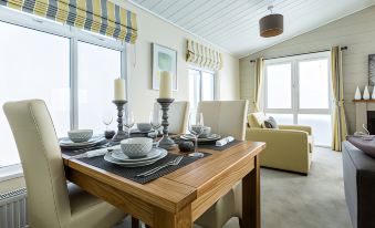 a dining table set with plates , silverware , and wine glasses in a room with large windows at King's Lynn Caravan & Camping Park