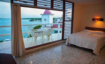 a hotel room with a large window offering a view of the ocean , a dining table , and a bed at Hotel Laguna Bacalar