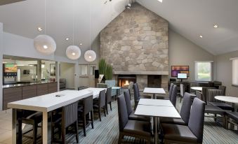 a modern , open - concept kitchen and dining area with a large stone fireplace , white table and chairs , and pendant lights at Sonesta ES Suites Providence - Airport