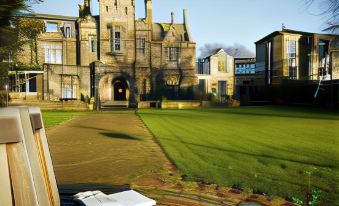 a grassy courtyard with a large building in the background , surrounded by trees and other greenery at Mercure Bradford Bankfield Hotel