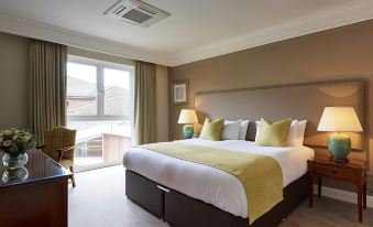 a large bed with a yellow blanket and white pillows is in a room with a window at Coldra Court Hotel by Celtic Manor