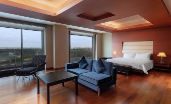 a modern hotel room with wooden floors , large windows , and comfortable furniture , including a blue couch and a black table at Le Méridien Coimbatore