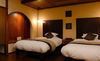 a hotel room with two beds , each made up with white sheets and pillows , in a wooden - walled room at Miyako