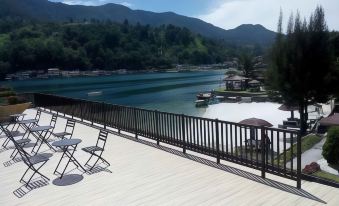 a wooden deck overlooking a lake , with several chairs and tables set up for outdoor dining at Khas Parapat