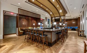 a modern hotel lobby with a long bar and wooden chairs , creating an inviting atmosphere at The H Hotel