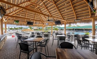 an outdoor dining area with several tables and chairs , as well as a bar and pool in the background at Ramada by Wyndham Sarasota Waterfront
