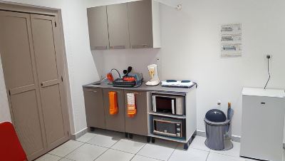 a small kitchen area with a stove , microwave , and various items on the counter , including cups , bottles , and towels at Vichy