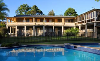 a large house with multiple balconies and windows is surrounded by a black fence , and a swimming pool in front of it at Bucketts Way Motel