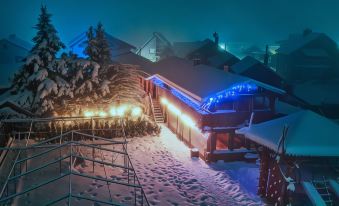 a snow - covered hillside with a building , possibly a house , lit up at night , creating a winter wonderland atmosphere at VeLa