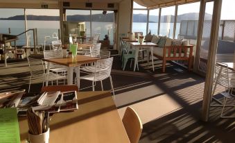 a modern , minimalist interior with large windows offering a view of the ocean , and white furniture on wooden tables and chairs at The Cove