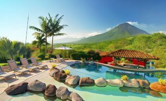 a large swimming pool with a tropical setting , umbrellas , and lounge chairs , surrounded by lush greenery and mountains at Hotel Mountain Paradise