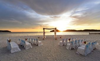a wedding ceremony taking place on a sandy beach , with the sun setting in the background at Pelangi Beach Resort & Spa, Langkawi