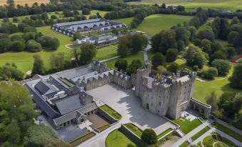 aerial view of a castle surrounded by a field , with a large building in the background at Kilkea Castle